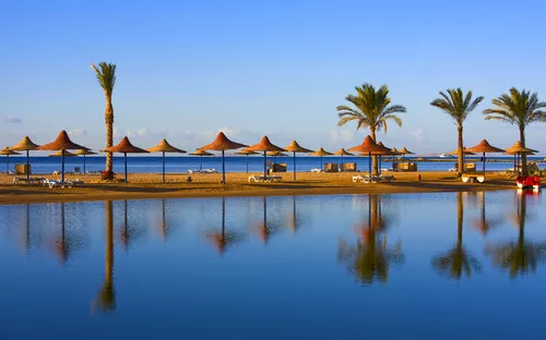 Strand mit Palmen, Sonnenschirmen und ruhigem Wasser bei klarem Himmel