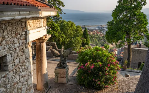 Steinbalkon mit Blick auf das Meer, umgeben von Bäumen und historischen Gebäuden.