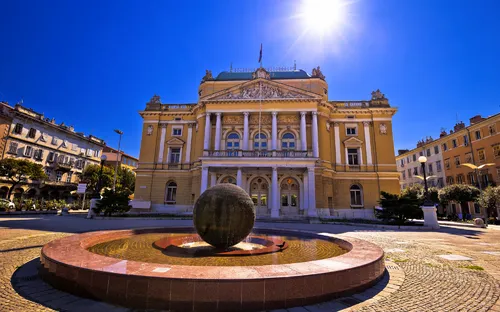 Historisches Gebäude mit Brunnen und Kugel in sonniger Umgebung.