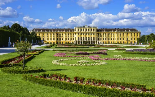 Schloss Schönbrunn mit gepflegtem Garten und blauem Himmel im Hintergrund.