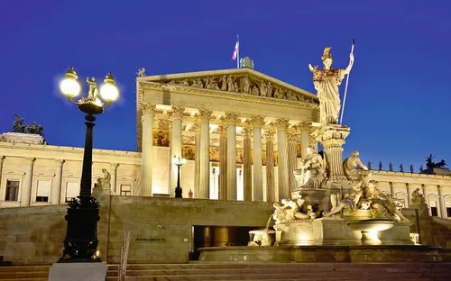 Beleuchtetes Parlamentsgebäude in Wien bei Nacht mit der Pallas-Athene-Statue im Vordergrund.