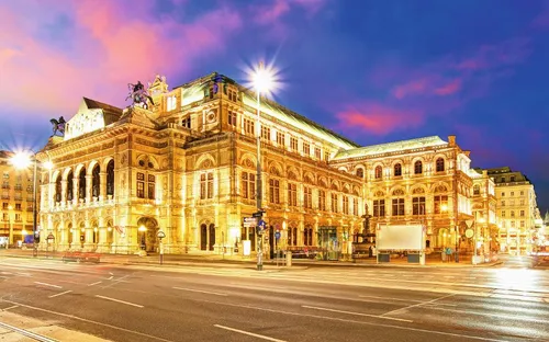 Opernhaus bei Nacht beleuchtet mit einem bunten Himmel im Hintergrund.