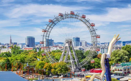 Riesenrad in einem Freizeitpark mit Stadtblick im Hintergrund an einem sonnigen Tag.
