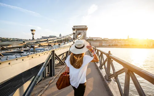 Frau mit Hut geht über eine Brücke bei Sonnenuntergang.