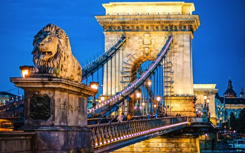 Kettenbrücke bei Nacht mit Löwenstatue und beleuchteten Lampen.