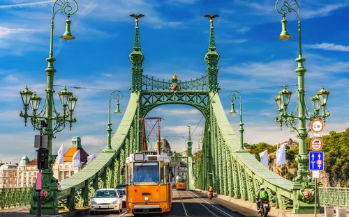 Grüne Brücke mit gelber Straßenbahn und Fußgängern am Tag.