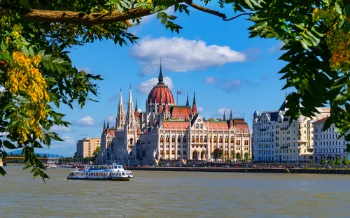Parlamentsgebäude von Budapest, Ungarn, am Ufer der Donau, umrahmt von Bäumen im Vordergrund.