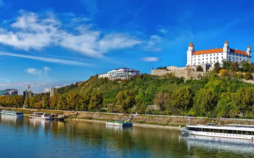 Burg auf Hügel über Fluss mit Schiffen an einem klaren, sonnigen Tag.