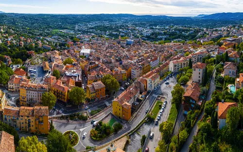 Luftaufnahme einer mediterranen Stadt mit roten Dächern und viel Grün in der Umgebung.
