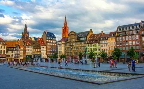 Historischer Platz mit Brunnen und Fachwerkhäusern bei bewölktem Himmel.