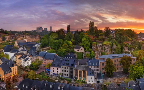 Panoramablick auf eine Stadtlandschaft bei Sonnenuntergang mit Brücke und grünen Bäumen.