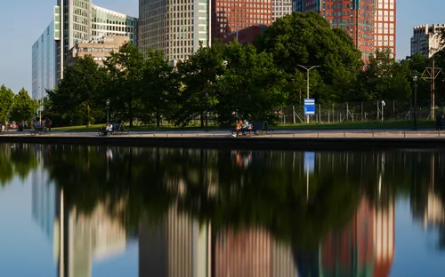 Moderne Gebäude mit Bäumen davor spiegeln sich im Wasser.