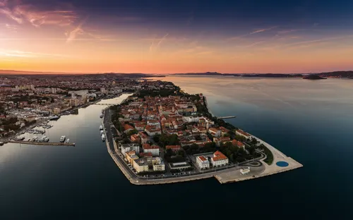 Luftaufnahme einer Halbinsel mit Stadt am Meer bei Sonnenuntergang.