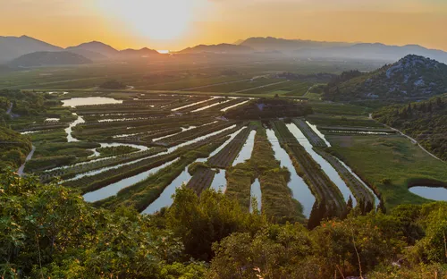 Sonnenuntergang über Landschaft mit Flüssen und Feldern in hügeliger Umgebung.