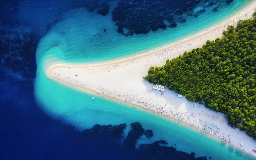 Luftaufnahme eines schmalen Strands mit klarem, blauem Wasser und grünen Bäumen.