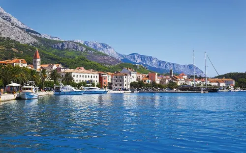Küstenstadt mit Yachten und Bergen im Hintergrund.