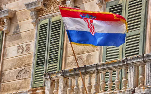 Kroatische Flagge weht an einem Balkon vor einem Gebäudebalkon mit grünen Fensterläden.