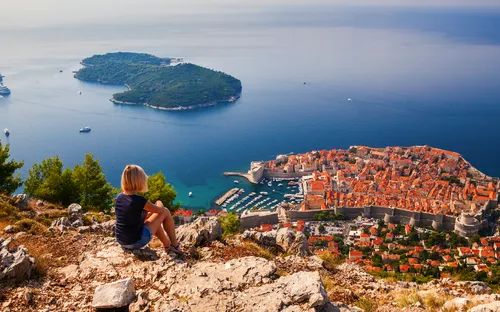 Frau blickt auf Dubrovnik von einem Hügel, im Hintergrund das Meer und Inseln.