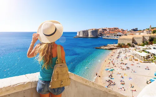 Frau in Sommerkleidung blickt auf Küste und Altstadt am Meer