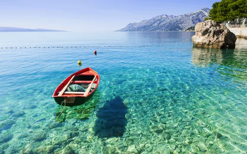 Rotes Boot auf klarem, türkisfarbenem Wasser vor einer felsigen Küste.