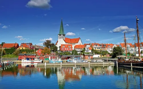 Hafenstadt mit bunten Häusern und Kirche, Boote im Wasser, blauer Himmel.