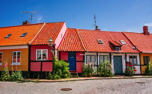 Bunte Fachwerkhäuser mit roten Dächern in einer sonnigen, gepflasterten Straße.