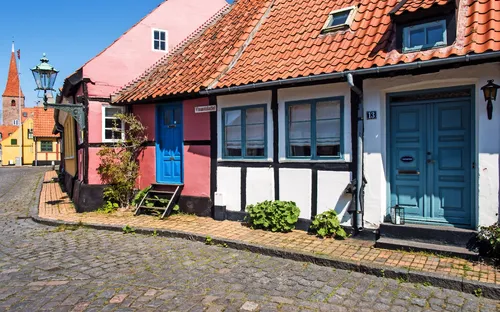Bunte Fachwerkhäuser an einer kopfsteingepflasterten Straße bei Sonnenschein.