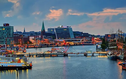 Hafenansicht bei Sonnenuntergang mit Gebäuden und Schiffen im Wasser.