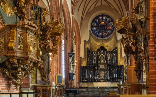 Innenraum einer reichen barocken Kirche mit Altar und buntem Rosettenfenster.