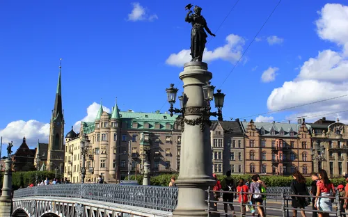 Personen überqueren eine historische Brücke in einer europäischen Stadt bei blauem Himmel.
