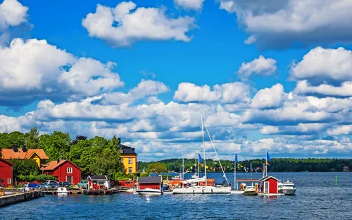Küstenlandschaft mit bunten Häusern und Segelbooten auf einem sonnigen Tag.