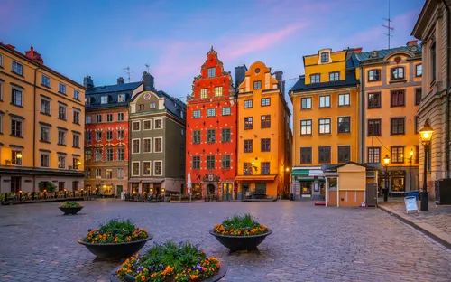 Ein Platz mit historisch bunten Gebäuden und Blumenkübeln bei Sonnenuntergang.