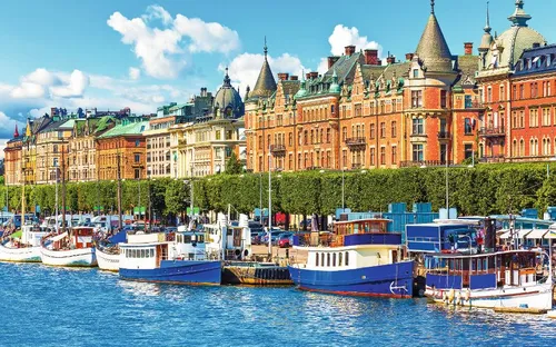 Boote am Wasser vor einer Reihe historischer Gebäude bei sonnigem Wetter.