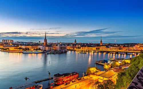 Stadtansicht mit beleuchteter Uferpromenade und Gebäude im Abendlicht.