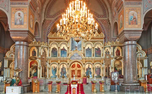 Innenansicht einer orthodoxen Kirche mit großem Kronleuchter und Ikonostase.