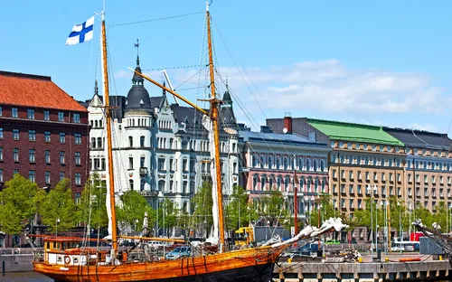 Segelschiff im Hafen vor historischen Gebäuden und finnischer Flagge.