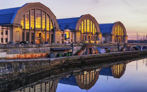 Drei beleuchtete Gebäude am Ufer eines Kanals bei Sonnenuntergang.