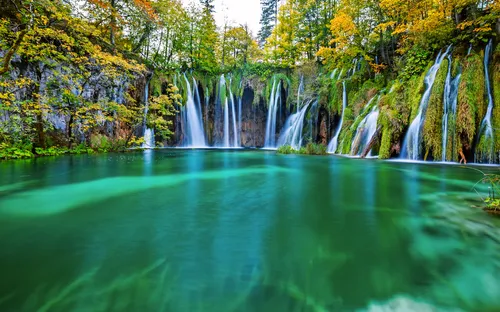 Wasserfall mit klarem grünem Wasser und Herbstbäumen im Hintergrund.