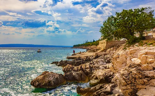 Küste mit felsiger Landschaft und blauem Meer unter wolkigem Himmel.