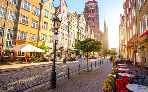 Straße mit bunten Häusern und Außencafé bei Sonnenschein in einer Altstadt.