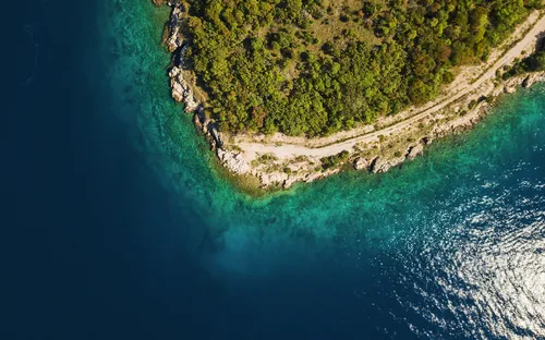 Luftaufnahme einer Küstenlinie mit klarem, blauem Wasser und grüner Vegetation.