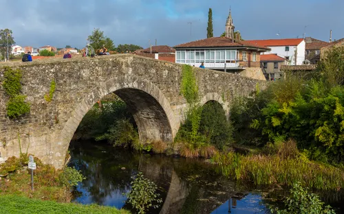 Steinbrücke über einen Fluss in einer ländlichen Gegend mit Gebäuden im Hintergrund.