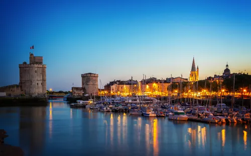 Yachthafen in La Rochelle bei Sonnenuntergang mit beleuchteten Türmen und Altstadt.