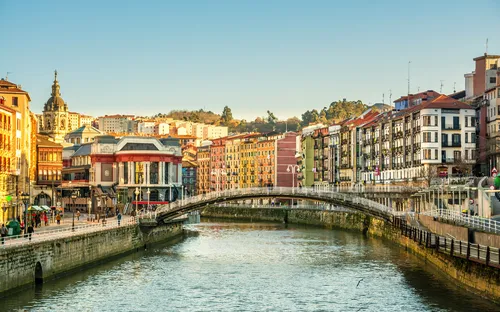 Fluss mit Brücke und bunten Häusern im Sonnenlicht einer Stadt.
