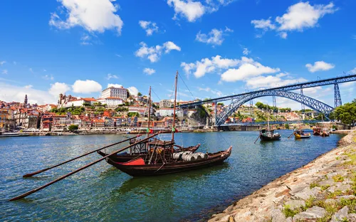 Boote auf einem Fluss vor einer Brücke in einer Stadtlandschaft mit blauem Himmel.