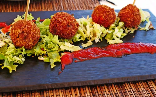 Frittierte Bällchen auf Salat mit roter Soße auf Schieferplatte serviert.