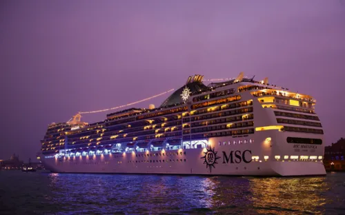 Kreuzfahrtschiff auf beleuchtetem Wasser bei Sonnenuntergang.
