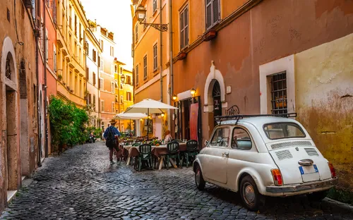 Eine gepflasterte Gasse mit Café und geparktem weißen Auto.
