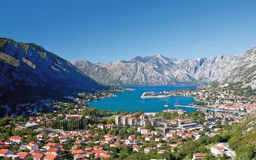 Küstenstadt mit Hafen, Bergen im Hintergrund und blauem Himmel.