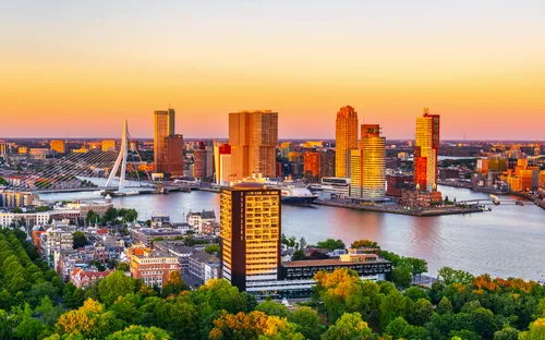 Skyline von Rotterdam bei Sonnenuntergang mit Erasmusbrücke und Hochhäusern am Wasser.